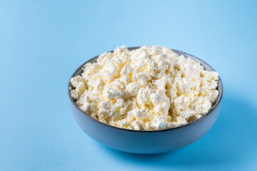 Organic cottage cheese in a blue ceramic bowl on blue background. Dairy products for the healthy breakfast. Healthy food concept. Hard light