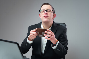 Down syndrome businessman sipping his coffee in the office, sitting at his laptop