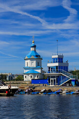 Fototapeta na wymiar Summer landscape with a view of a white church with a blue dome and a boat dock on the bay.