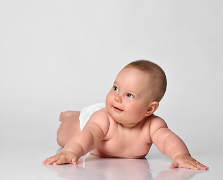 Happy portrait Six month old baby girl in a diaper, lying down and looking up with interest, arms outstretched to the sides. on white background