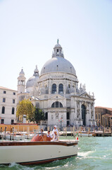 The Basilica Di Santa Maria Della Salute view From Grand Canal and retro design motor boat with passengers in the foreground.
