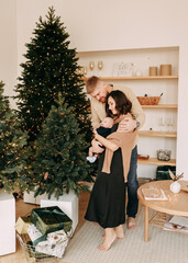 concept of Christmas holidays. A happy young family with one small child in casual clothes celebrate the new year near the Christmas tree in a cozy house. Parents and baby spend time together