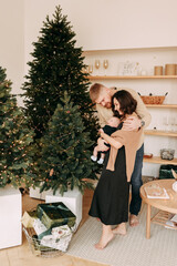 concept of Christmas holidays. A happy young family with one small child in casual clothes celebrate the new year near the Christmas tree in a cozy house. Parents and baby spend time together