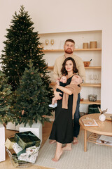 concept of Christmas holidays. A happy young family with one small child in casual clothes celebrate the new year near the Christmas tree in a cozy house. Parents and baby spend time together