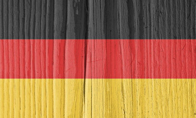 The flag of Germany on dry cracked wooden surface. It seems to flutter in the wind. Background or wallpaper with German national symbol. Hard sunlight with shadows on old wood
