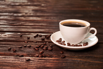 Coffee cup on old wooden table with cofee beans on plate, front view with copy space.