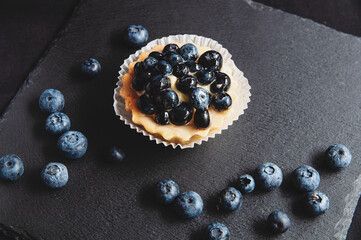 Tart with blueberries is on a black background of natural stone.