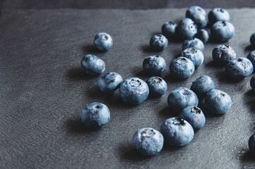 Blueberries scattered on a black background of natural stone.