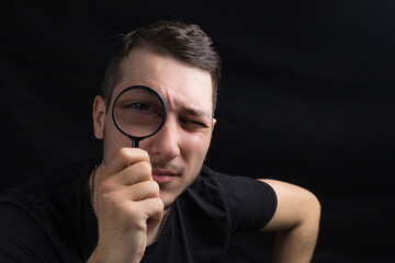 Young handsome man and a magnifying glass on black background in low key. Search symbol....