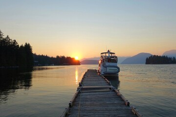 A boat tied to a dock with no other boats around it, at sundown, surrounded by beautiful calm ocean...