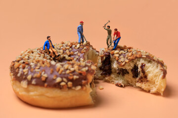 miniature workesr figures with hammers working on chocolate donut with nuts isolated on brown...