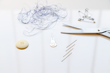 Macro close-up of a button, threader and needles next to tangled threads, scissors and safety pins, against white background