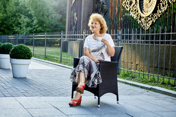 Senior woman on bench drinks coffee in city garden.