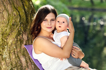 Mother and little child sits near tree in park during walking.