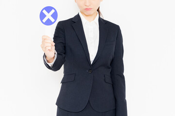 白背景の前に立って、NGのジェスチャーをするスーツを着たビジネスウーマン