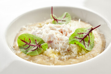 Risotto with crab meat in white restaurant plate. Garnished with Parmesan cheese and green leaves. Delicious crab meat risotto with white sauce isolated on white background. Rice with seafood.