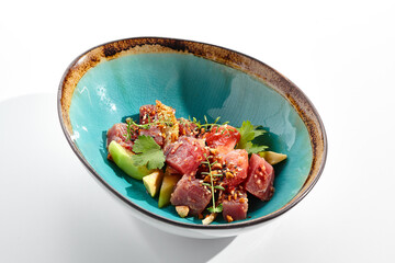 Tuna and avocado salad bowl. Blue salad bowl isolated on white background. Salad garnished with micro greens and sesame, chopped tuna, sliced avocado and parsley green leaf. Raw tuna with spicy sauce.