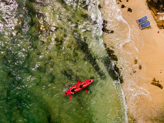 Fototapeta premium The top view of two tourist paddling their red kayak at the beatiful blue seashore and two beach chair in summer