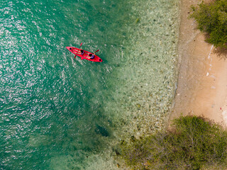The top view of two tourist paddling their red kayak at the beatiful blue seashore in summer