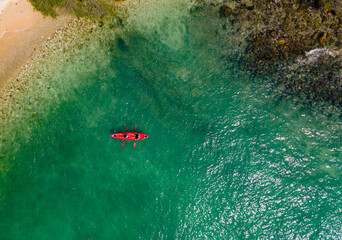 Fototapeta premium The top view of two tourist paddling their red kayak at the beatiful blue seashore in summer