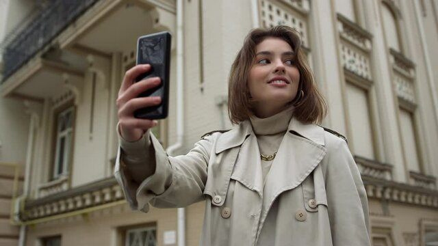 Smiling woman taking selfie on urban street. Girl pouting lips for phone camera.