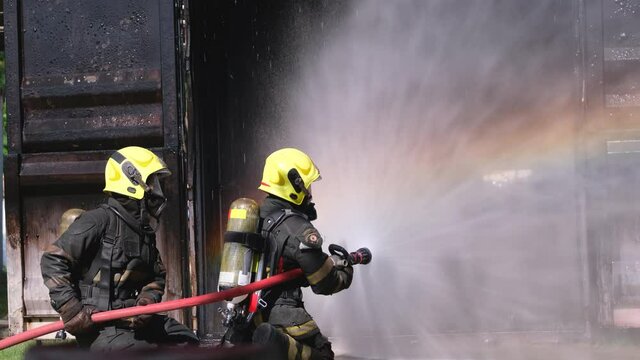 Fireman team spray water as circular around area in front of burning container with rainbow reflection during practicing of staff to preparation and ready to service people when disaster occur.
