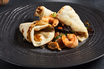 Salad with shrimp and pita bread. Seafood and vegetable on black ceramic plate.  Gourmet, restaurant healthy food concept. Dark textured table