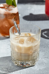 White russian cocktail is a cocktail made from coffee liqueur and vodka. Cocktail glass with spoon on vintage table with sunshine and long shadow. Classic cocktail collection. - obrazy, fototapety, plakaty