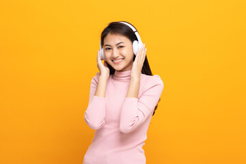 Cheerful asian female teenager listen to the music with white headphone dancing on isolated yellow background. Beautiful young woman in hand touch a wireless headphone having fun with music.