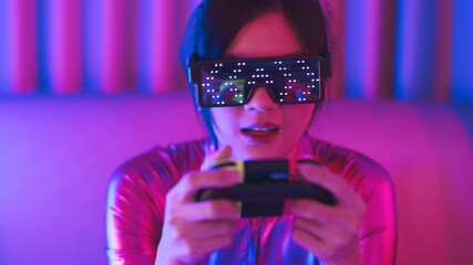 Young asian woman is using virtual reality headset. Neon light studio portrait. Concept of virtual reality, simulation, gaming and future technology.Asian woman play game in bedroom.