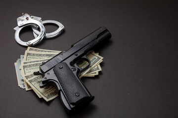 Pistol handcuffs and American dollar banknotes on black background.