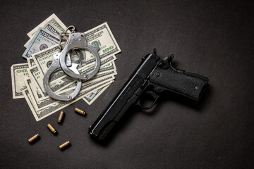 Pistol handcuffs and American dollar banknotes on black background.