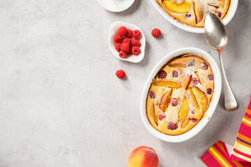 Fototapeta na wymiar Traditional french pie clafoutis with fresh summer peaches and raspberry. Light- gray stone background, top view
