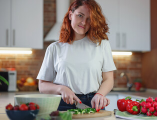 Beautiful redhair young woman is preparing vegetable salad in the kitchen. Healthy vegan Food. Dieting Concept. Cooking At Home. Food blogger concept