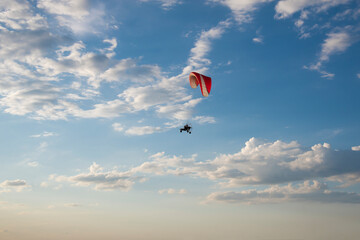 The silhouette of a motorized paraglider against a blue cloudy sky. The concept of extreme sports