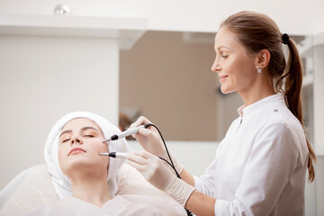 Young woman having stimulation microcurrent procedure for lifting skin face treatment from spa clinic