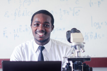 African scientist teacher is teaching science classes with using microscope in the...