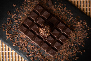 Brazilian gourmet brigadier. Small chocolate ball coated by dark chocolate flakes over a chocolate bar on a black slate board over a bamboo mat.