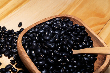 Black soy beans in wooden scoop isolated on wood table background.