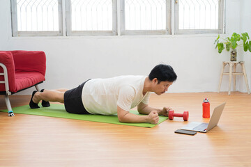 Online workout. Young man doing plank exercise with online tutorial at home