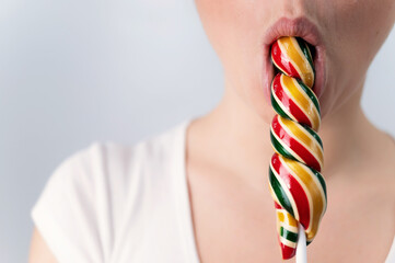 Close-up portrait of a woman sucking a long lollipop against a white background. Blowjob simulation