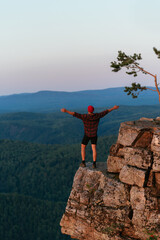 Obraz premium Back view of a man standing against the background of mountains with his arms outstretched. The man in the mountains raises his hands. Man on the background of mountains. Travel to the mountains