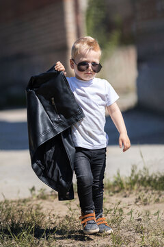A blond guy with dark glasses and a leather jacket.The little boy is stylishly dressed in a rock style.Cute baby looks like a celebrity.A child on a walk on a sunny day.The idea of a children's photo