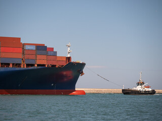 Large Container Ship Towed into Port by a Small Tugboat