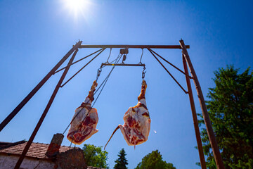 Two fresh pork hams hangs hooked by hooks on metal construction, carrier