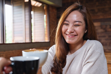 Portrait image of a beautiful young asian woman and a man clinking coffee mugs together in cafe