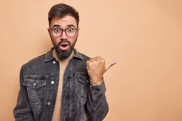 Impressed bearded handsome man points thumb away recommends follow website click on banner gasps...