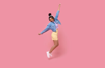 Happy beautiful Asian teen woman in yellow glasses listening music in headphones and dance on pink background..