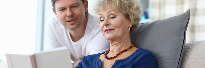 Elderly woman reads book with her adult son