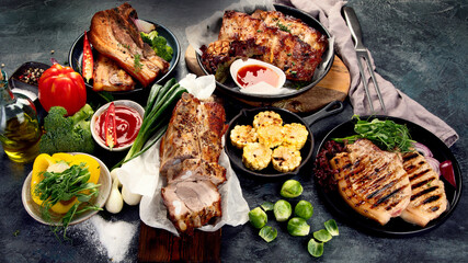 Assortment of grilled pork meat with vegetables on dark grey background.